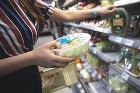Femme tenant une salade préfabriquée dans une épicerie.